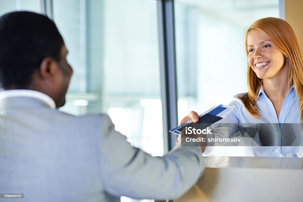 Returning documents Attractive young woman giving passport and ticket back to businessman at airport check-in counter Adult Stock Photo