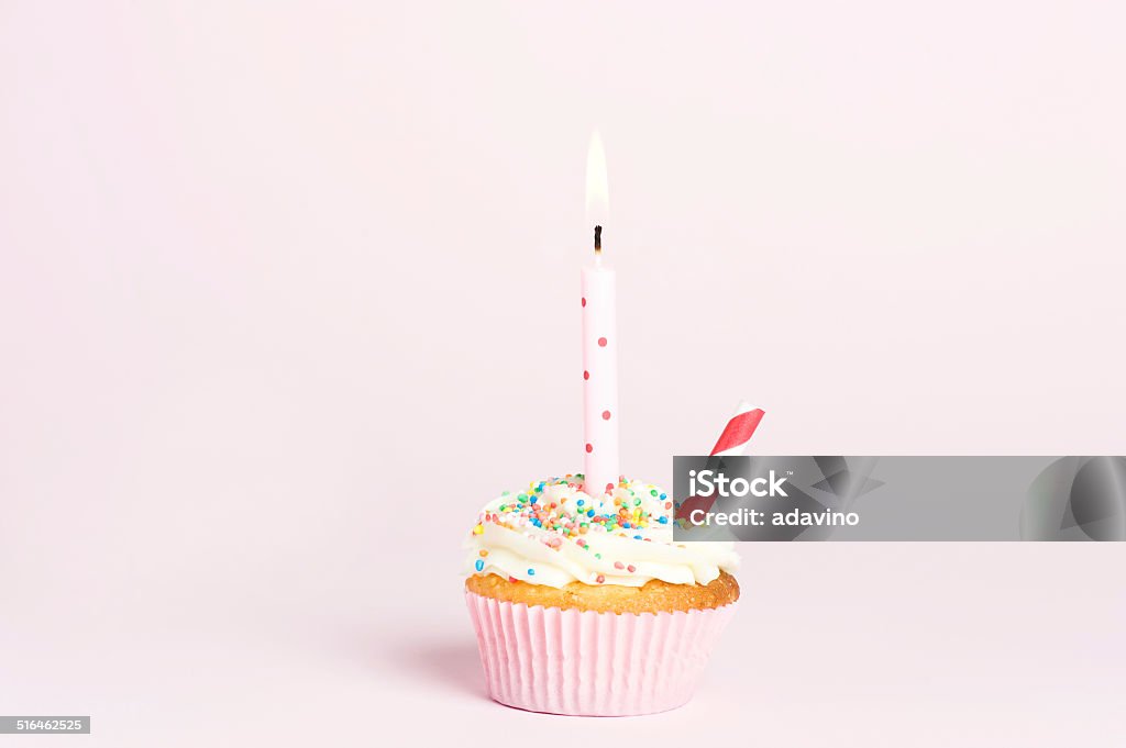 Cupcake with candle Cupcake, with buttercream flavor and sprinkles on top of sugar cream in a pink paper patty pan on a pink background with a birthday candle on top lit up Baked Stock Photo