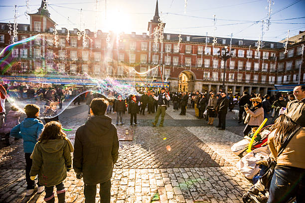 Madrid, Spain  - December 22, 2013: Crowds of people visiting Christmas Market on Plaza Mayor, Madrid. Man on foreground photographing with small digital camera. Backlit shot.