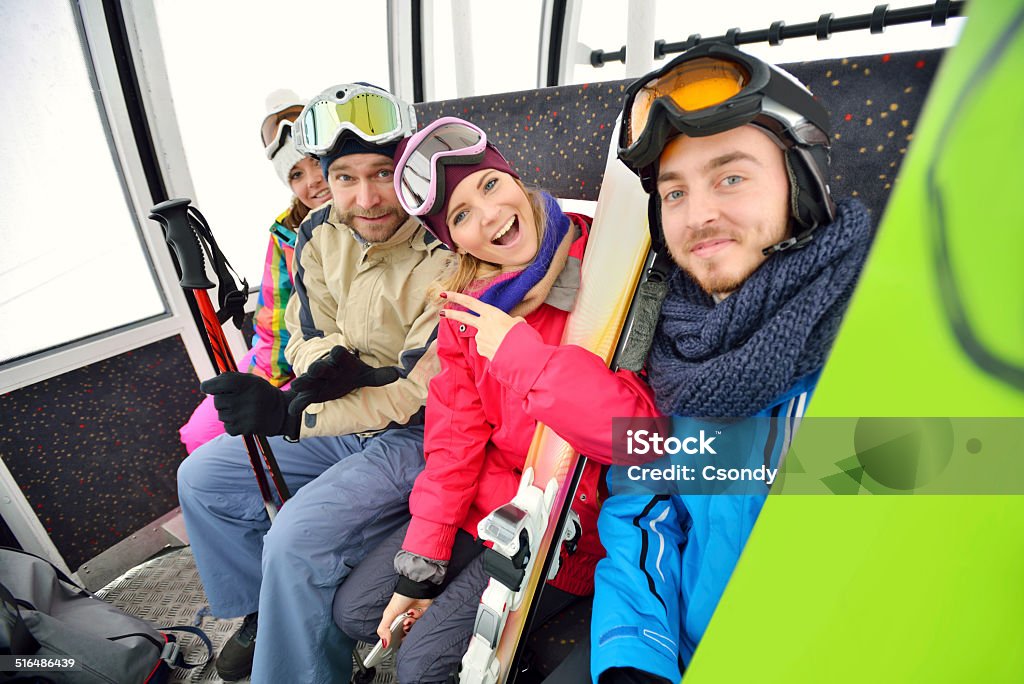 Young snowboarding team in the ski lift Young happy people sitting in the ski lift with snowboard and ski. Friendship Stock Photo