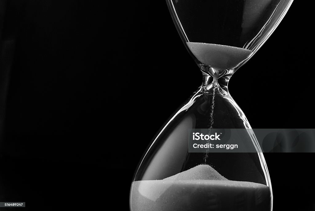 Sand running through the bulbs of an hourglass Sand running through the bulbs of an hourglass measuring the passing time in a countdown to a deadline, on a dark background with copyspace Hourglass Stock Photo