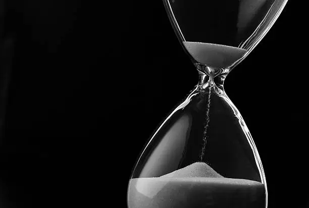Sand running through the bulbs of an hourglass measuring the passing time in a countdown to a deadline, on a dark background with copyspace