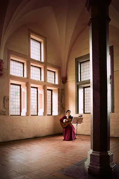 A woman playing a guitar while sitting in a large open room in Malbork Castle, Poland.