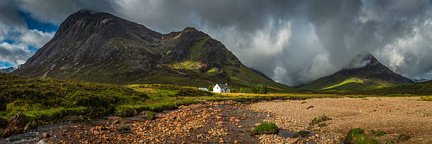 Mountain cottage below dramatic wilderness peaks panorama Glencoe Highlands Scotland Traditional white-washed crofter's cottage in idyllic Highland glen below dramatic cloudscape sweeping over wild mountain peaks, Scotland, UK. ProPhoto RGB profile for maximum color fidelity and gamut. glencoe scotland photos stock pictures, royalty-free photos & images
