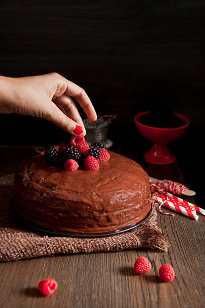 istock Woman's hand putting a blackberry on a chocolate cake 516510665