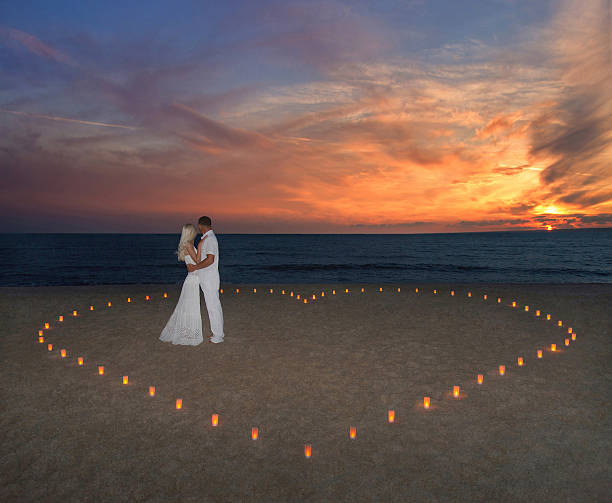 młoda para w sercu świece na plaży przed zachodem słońca w morzu - couple engagement valentines day heart shape zdjęcia i obrazy z banku zdjęć