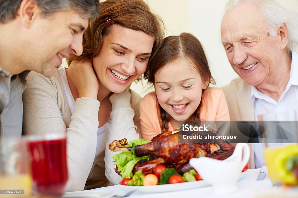 Hunger Portrait of joyful people looking at roasted turkey by festive table Family Stock Photo