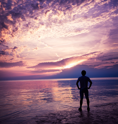 Silhouette of a Young Man Enjoying Sunset at Sea. Beautiful Nature Background. Toned Photo with Copy Space.