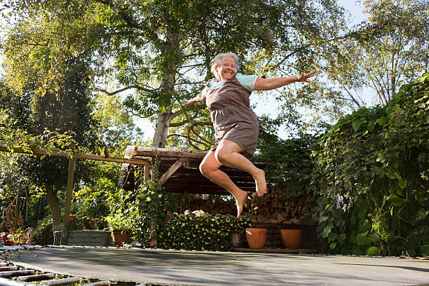 cheerful senior woman, 60 yeas old, with overweight, but enjoying to jump on trampoline in garden, 