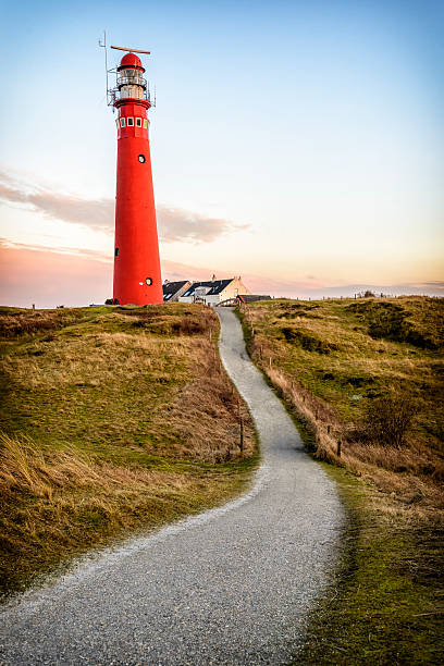 Lighthouse in the dunes Path leading to a red lighthouse in the dunes with fishermen's cottages. friesland netherlands stock pictures, royalty-free photos & images