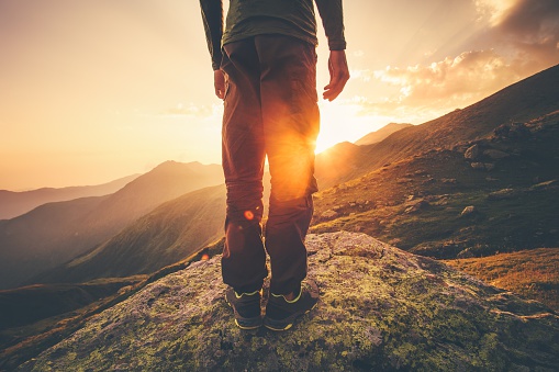 Young Man Traveler feet standing alone with sunset mountains