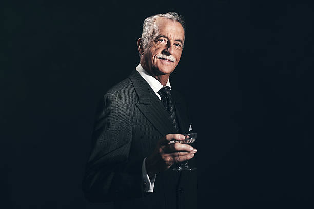 улыбающаяся ретро - 1940 s старший бизнесмен, держа бокал для шампанского. - senior men businessman portrait dark стоковые фото и изображения