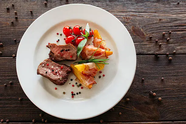 Medium rare pork steak with fresh vegetables. Food photography of pork steak with potatoes and tomatoes cherry. Tasty cook meat with vegetables on dark wooden background. 