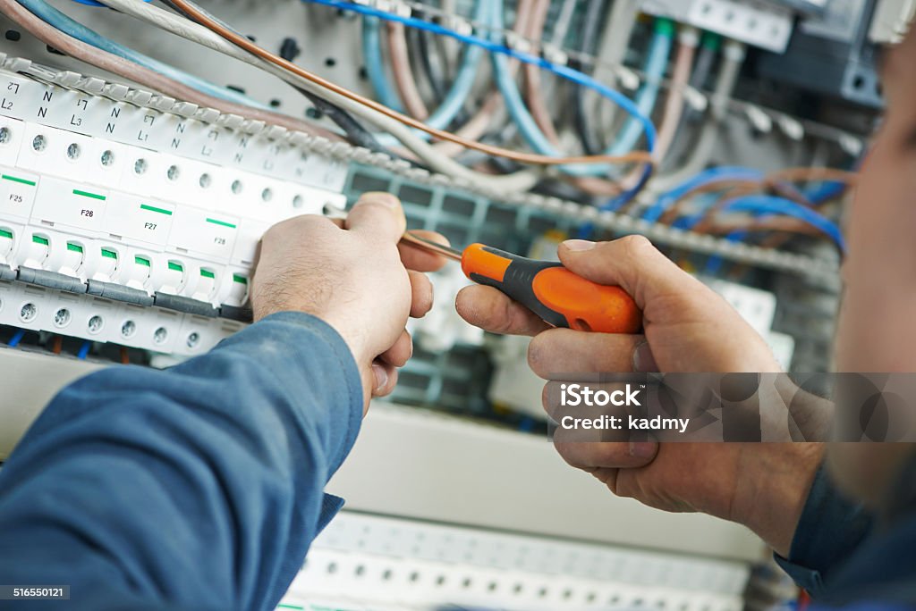 electrician work Hands of electrician with screwdriver tighten up switching electric actuator equipment in fuse box Electrician Stock Photo