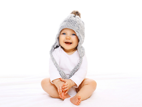 Happy smiling baby in grey knitted hat on a white background