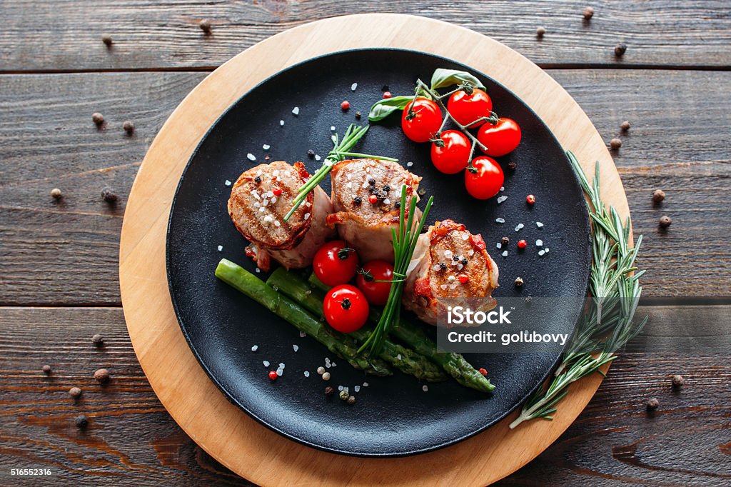 Grilled pork with vegetables and spices Grilled pork dish with fresh vegetable spices. Food photographyof grilled pork medallions with herbs and spices. Tasty cook meat with  vegetables on dark wooden background.  Plate Stock Photo