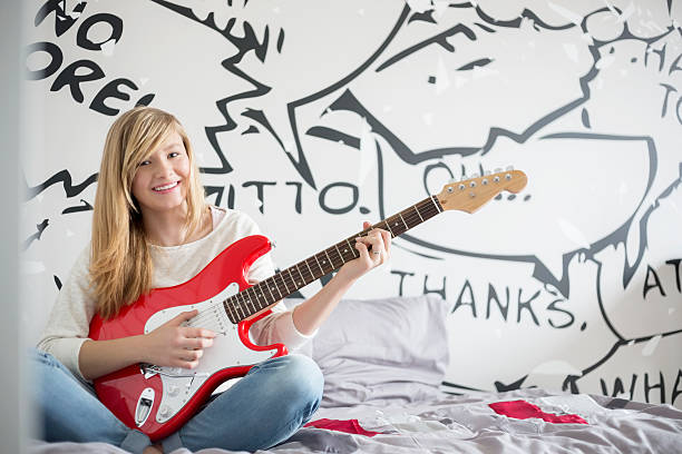 Family at Home Full-length portrait of teenage girl playing guitar in bedroom 15 year old blonde girl stock pictures, royalty-free photos & images