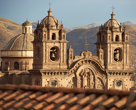 Twin towers and dome of the historic Iglesia de la Compania seen across the red rooftops of Cusco in Peru. The church dates back to 1571 and sits on top of an old Inca Palace.