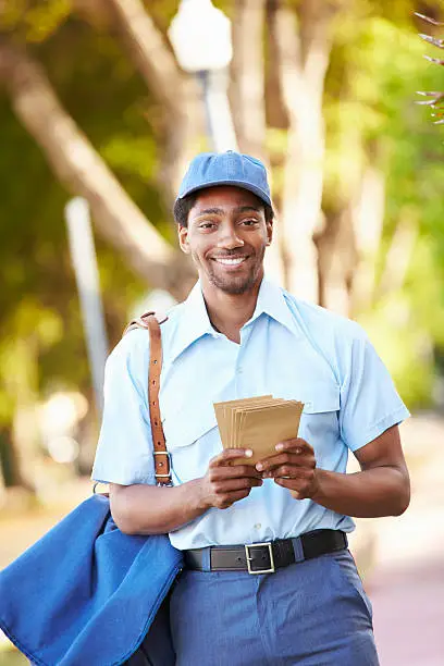 Mailman Walking Along Street Delivering Letters Smiling To Camera
