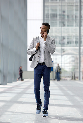 Full length portrait of a happy young man walking and talking on mobile phone