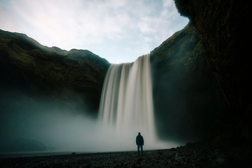 A man stands by Skogafoss at dusk, Iceland