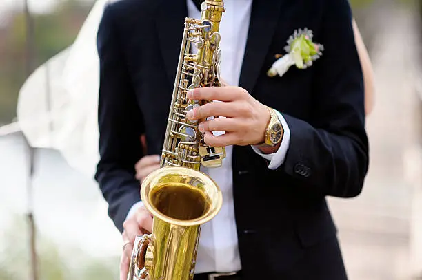 Photo of Hands of groom play on saxophone
