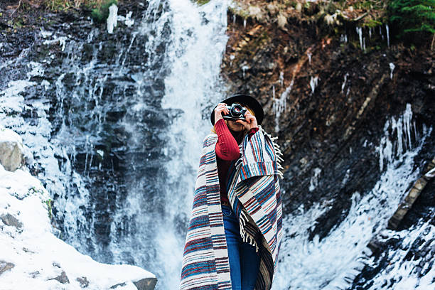 Young woman in plaid standing near the waterfall at winter 