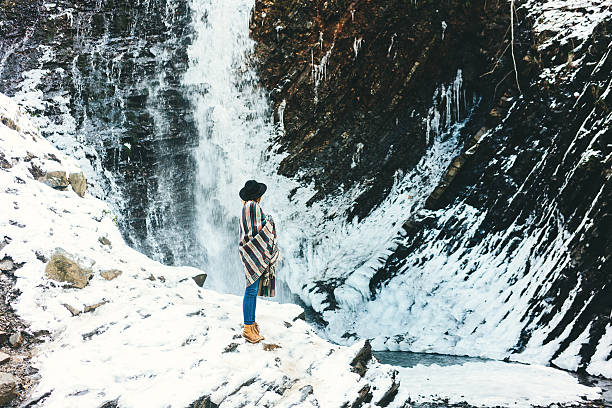 Young woman in plaid standing near the waterfall at winter 