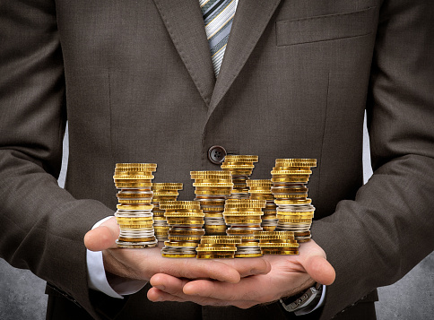 Businessman holding coins on grey wall background