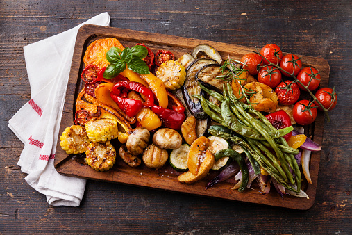 Grilled vegetables on cutting board on dark wooden background