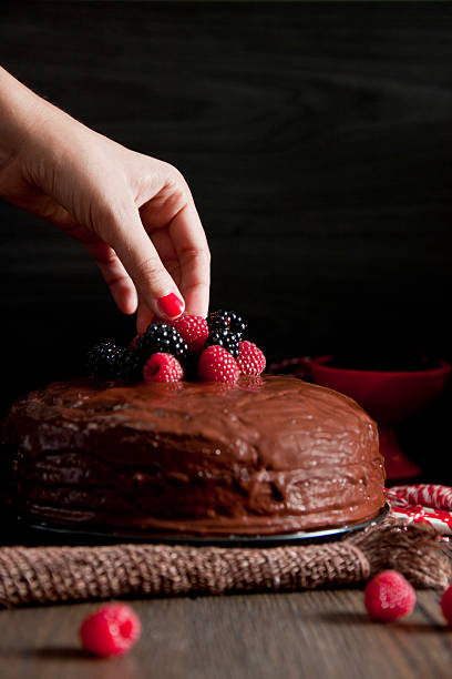 istock Woman's hand putting a blackberry on a chocolate cake 516633311