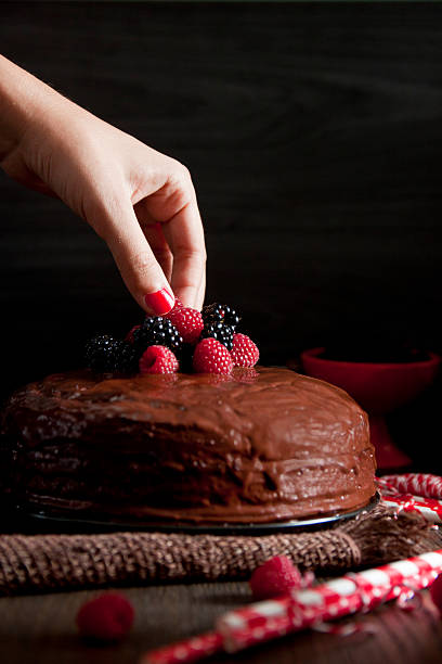 istock Woman's hand putting a blackberry on a chocolate cake 516633315