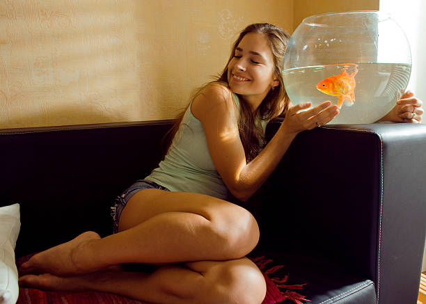 istock pretty woman playing with goldfish at home 516634533
