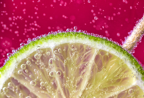 A slice of lime submerged in fizzy pink drink with bubbles.