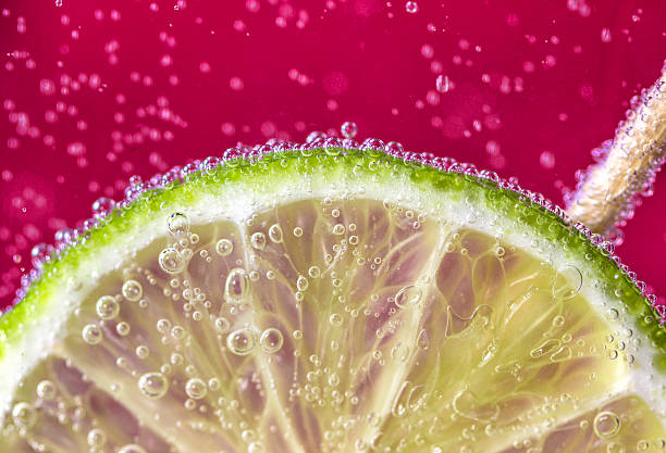 Fizzy Lime A slice of lime submerged in fizzy pink drink with bubbles. lime photos stock pictures, royalty-free photos & images
