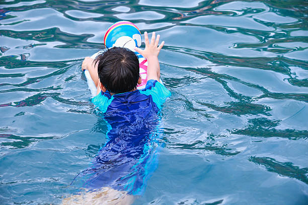 istock Back view of asian boy with kick board in pool. 516649392