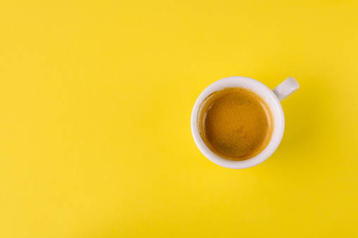 Small cup of coffee on bright yellow background, top view