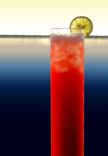 a red longdrink with slice of lemon in waterside evening ambiance