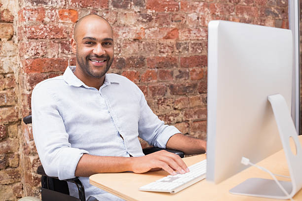 istock Worker in wheelchair working on computer smiles to camera 516653395