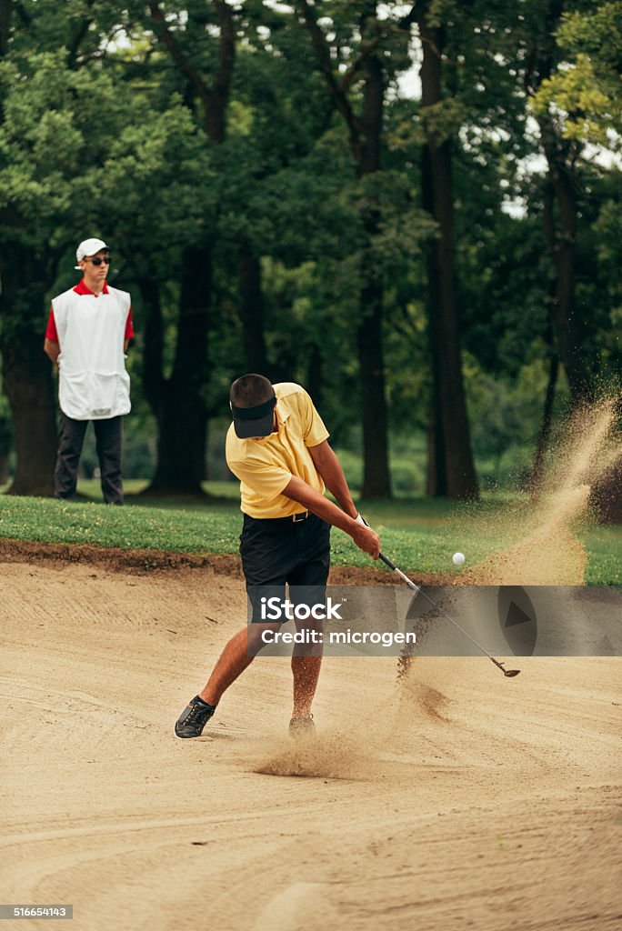 Golfer playing from sand bunker Golfer playing from sand bunker, caddy behind Golf Stock Photo