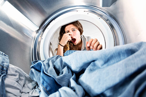 Laundry left in clothes dryer stinks! Unhappy woman holds nose. In an unusual view from inside the clothes drier drum, we see a horrified young woman holding her nose as she looks at the laundry which must have been forgotten and now smells! unpleasant smell stock pictures, royalty-free photos & images