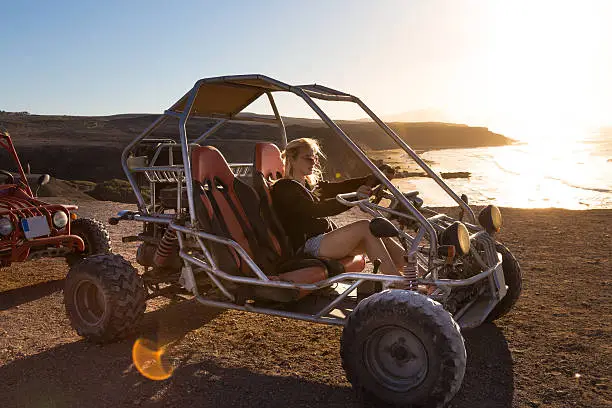 Active woman driving quadbike on dirt road by the sea in sunset.