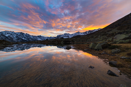 High altitude alpine lake in idyllic land once covered by glaciers. Reflection of snowcapped mountain range and scenic colorful sky at sunset. Wide angle shot taken on the Italian Alps at 2200 m asl.