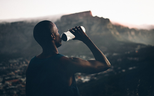 healthy fit african decent athlete drinking water after a fitness achievement with a great view of the mountain in the background in the late afternoon