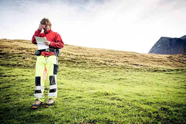 paramedic standing on alpine meadow, looking through documents.