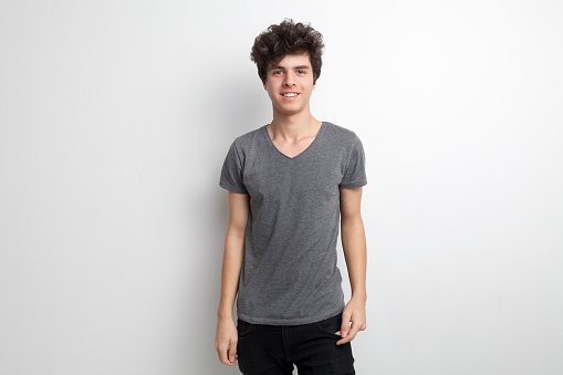 Surprised young man wearing denim shirt and white t-shirt pointing with index fingers at copy space and looking up. Studio shot, grey background.