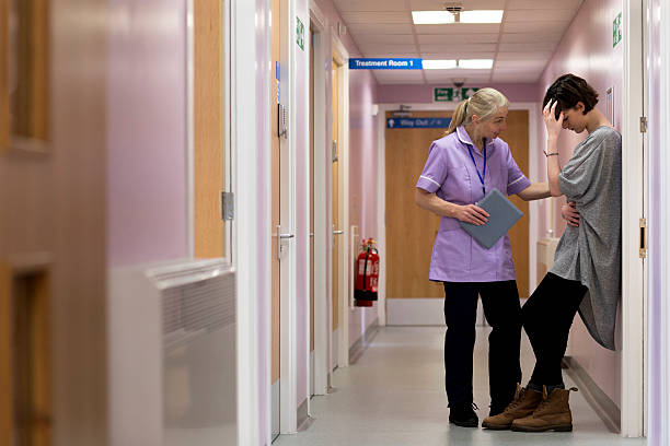 Don't worry, we will do everything we can Medical woman comforts young female adult as she stands with her back against to the wall in a hospital corridor. Head in her hand she looks very upset. personal perspective standing stock pictures, royalty-free photos & images