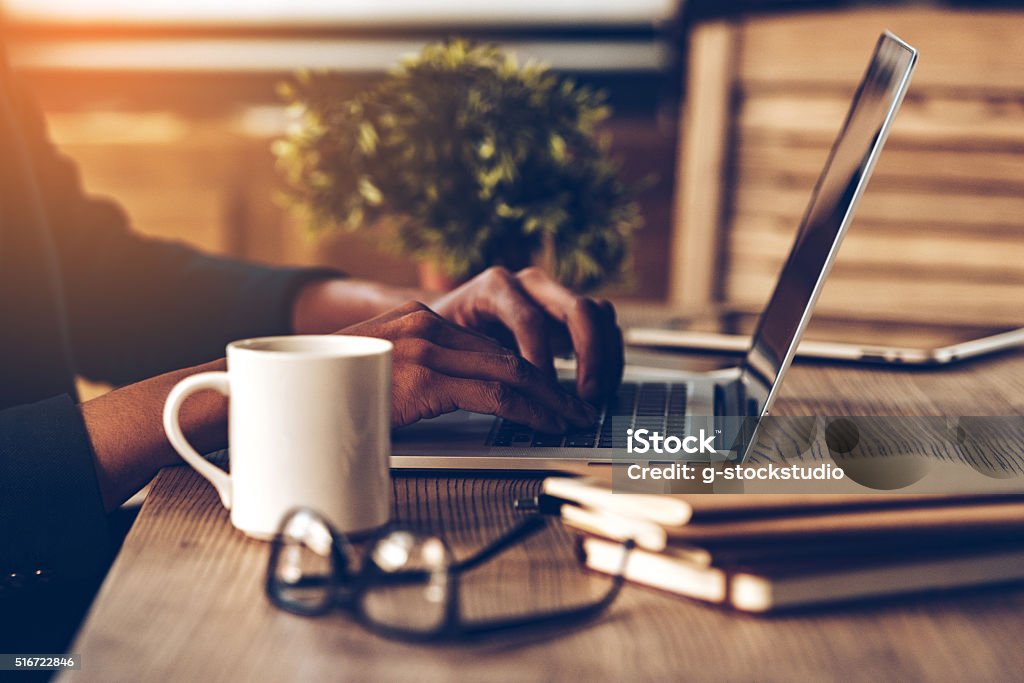 Working moments. Close-up side view part of young African man using laptop while sitting at his working place Lifestyles Stock Photo