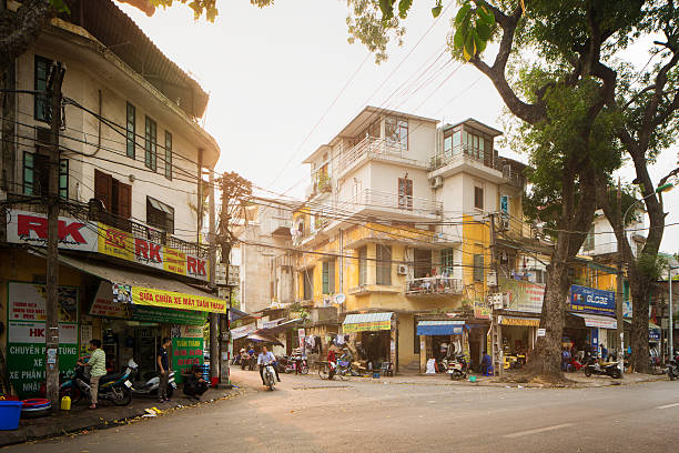 Hanoi Vietnam Nguyen Cong Tru street city life scene Hanoi, Vietnam - April 18, 2015: Hanoi Vietnam Nguyen Cong Tru street city life scene on a humid Spring day. People are going on about their day, riding motor scooters, sitting, eating, relaxing on their balconies, shopping in the first floor stores. Modern home improvements are built on top of older buildings. city street street corner tree stock pictures, royalty-free photos & images