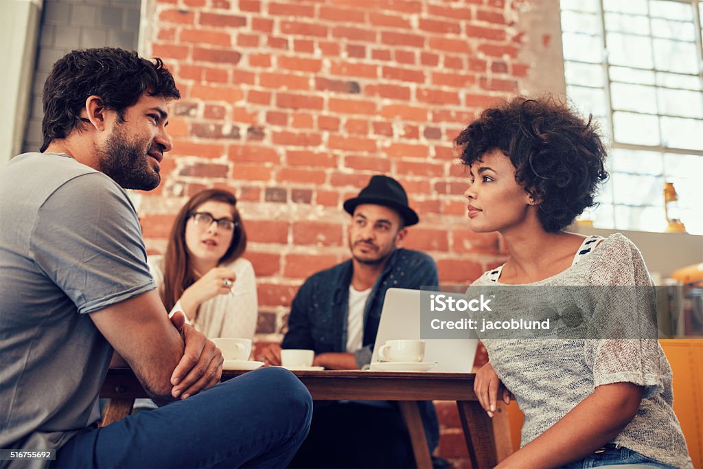 Young people meeting at a coffee shop Portrait of young friends sitting at a cafe table and talking. Group of young people meeting at a coffee shop. Casual Clothing Stock Photo